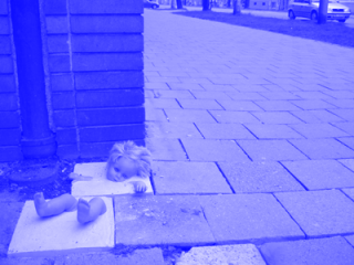 Panenka, Street-Art der Gruppe Crazy Crime. Eine in das Straßenpflaster einbetonierte Puppe